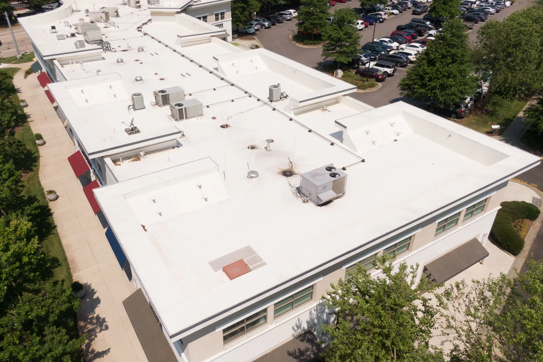 Aerial view of a multi-wing commercial complex with several connected white membrane roofs and a full car park.