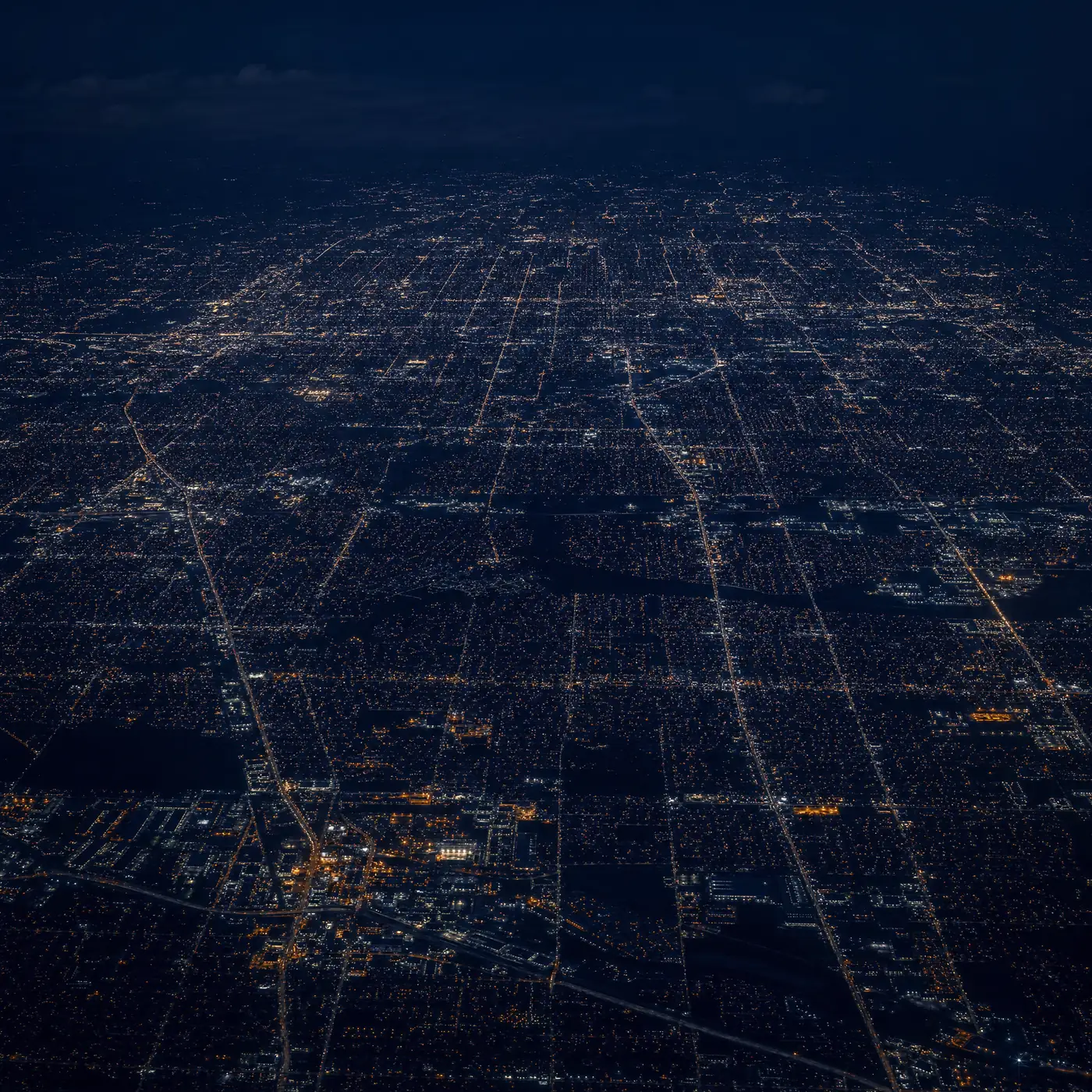 High-altitude night aerial of a vast American city grid lit up across the landscape
