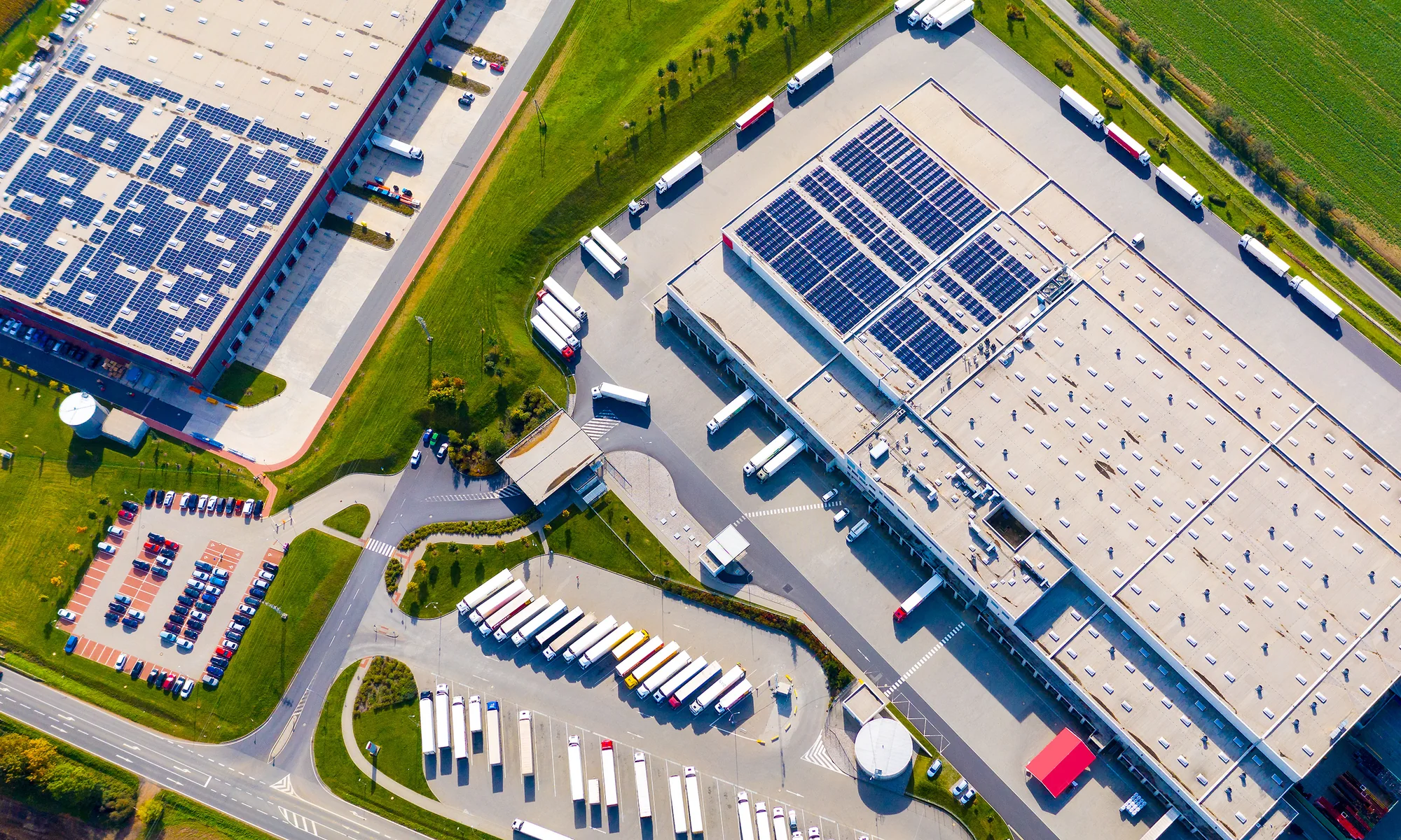 Aerial view of two large distribution centres with white membrane roofs, rooftop solar arrays and lines of trailers at the loading docks.