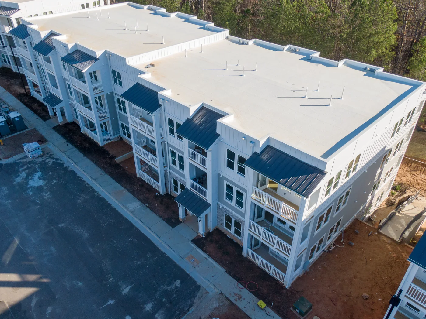 Aerial view of a three-storey multifamily building with a white TPO roof and metal balcony canopies.