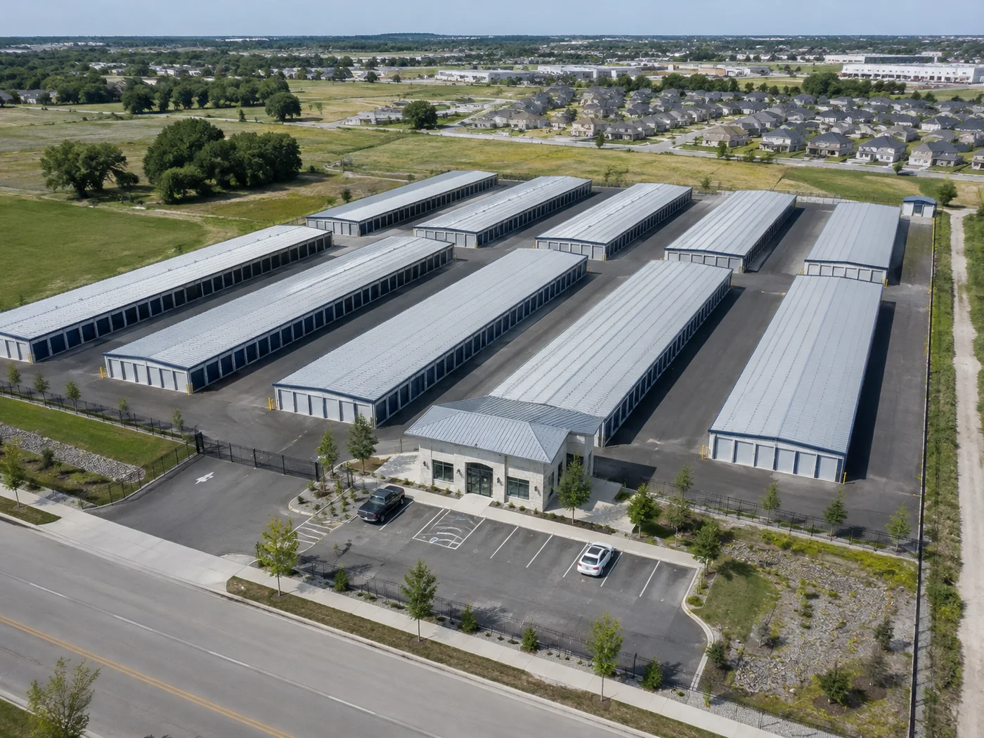 Aerial view of a multi-building self-storage facility with rows of long single-storey units, wide drive aisles and a gated office at the front.