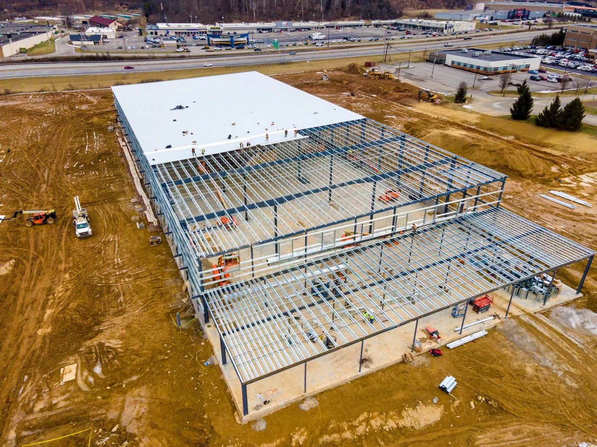 A large commercial building under construction with the steel frame exposed and the new roof deck being installed.