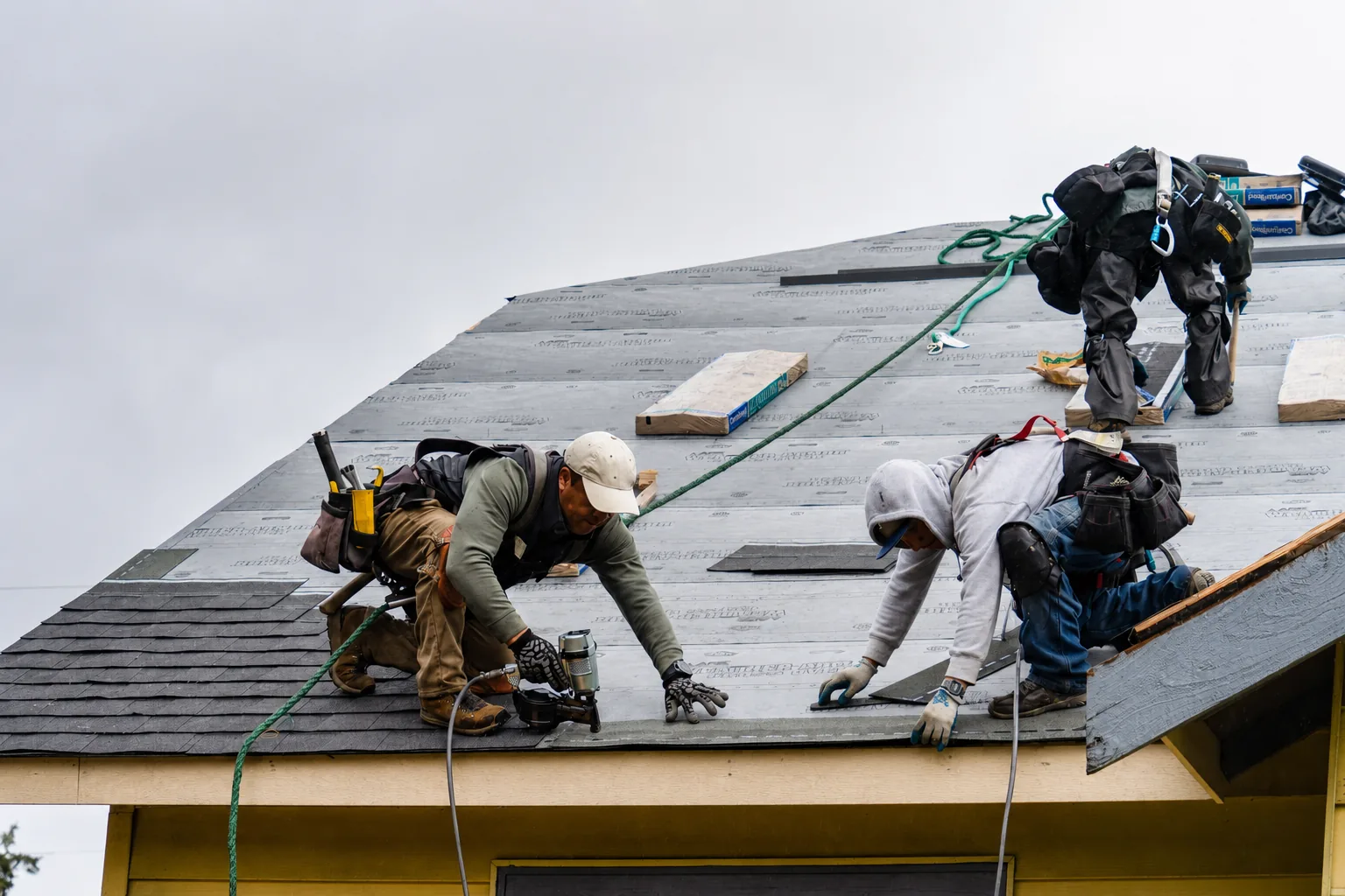 A Roofix crew installing shingles on a home, harnessed and working with nail guns